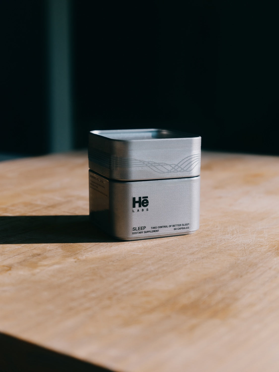 A silver container of Hē Labs Sleep supplement placed on a wooden table, promoting better sleep and recovery.