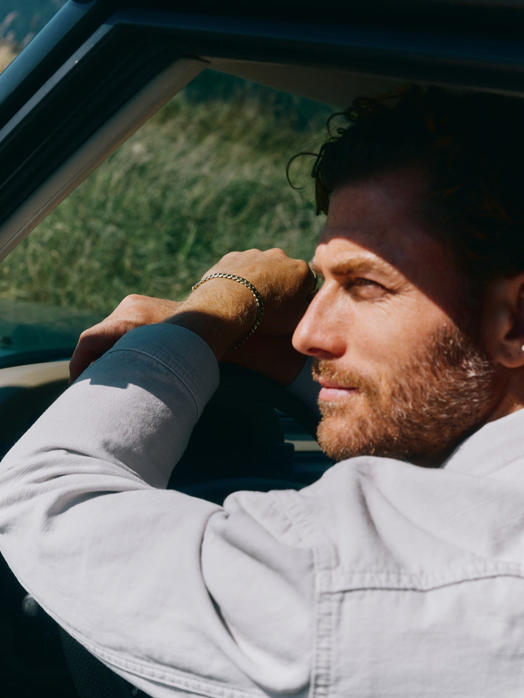 A thoughtful man sitting in a car, looking out the window with sunlight on his face, symbolizing reflection and strength.